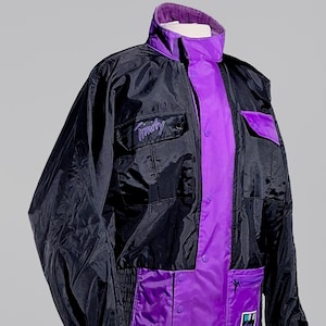 May include: Black and purple jacket with the name "Timothy" embroidered on the chest. The jacket has a high collar and multiple pockets. The interior lining is purple, and the exterior is black.