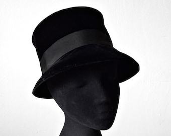 May include: A black velvet hat with a wide brim and a black ribbon around the crown.