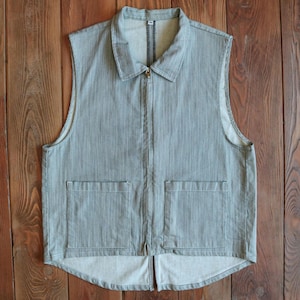 May include: A gray denim vest with a zipper closure and two large pockets. The vest has a pointed bottom and a collar.