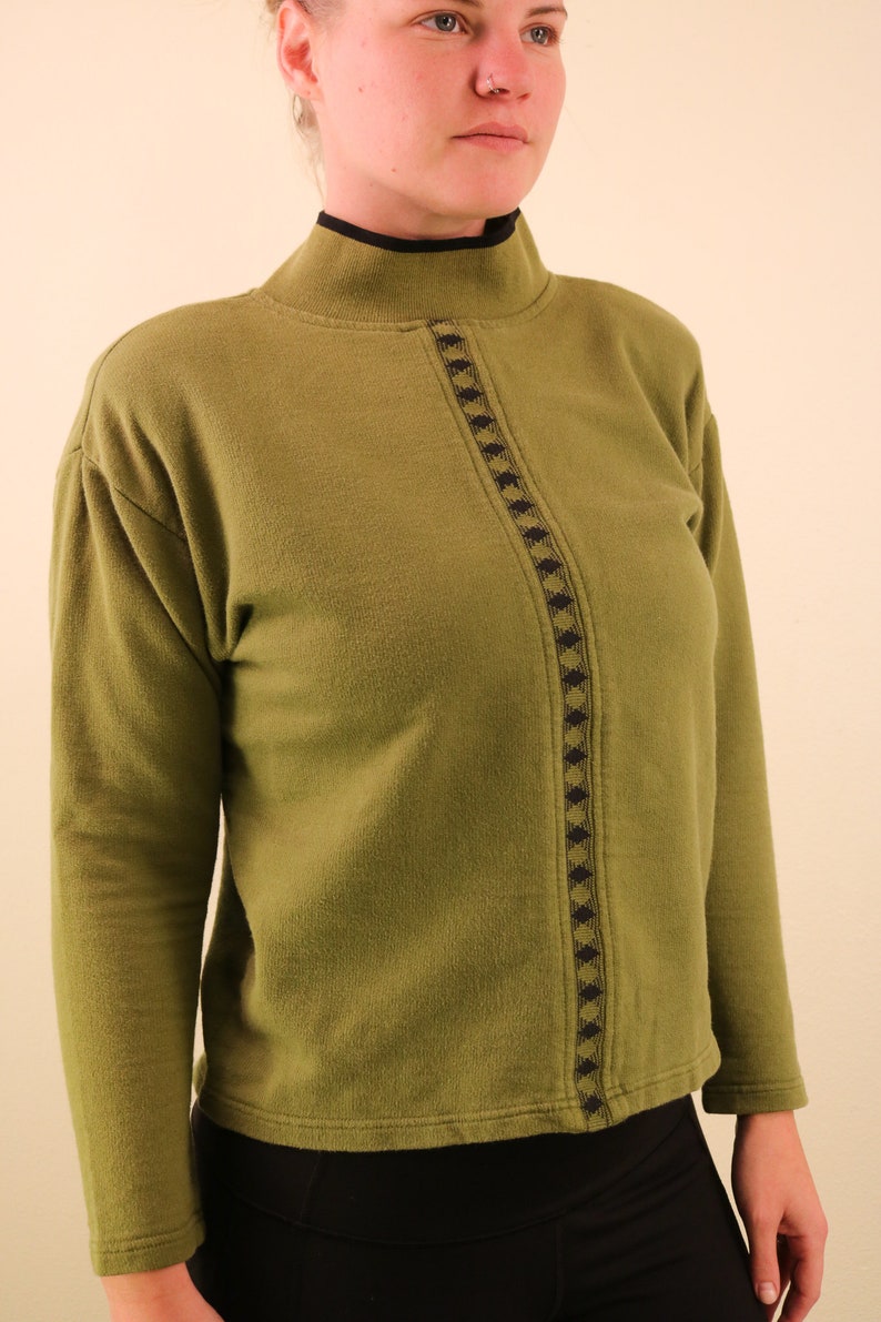 May include: A green mock neck sweater with a black and gold geometric pattern down the front.