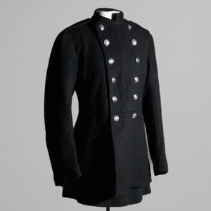 Puede incluir: Una chaqueta negra de doble botonadura con botones plateados. La chaqueta tiene un cuello alto y mangas largas.