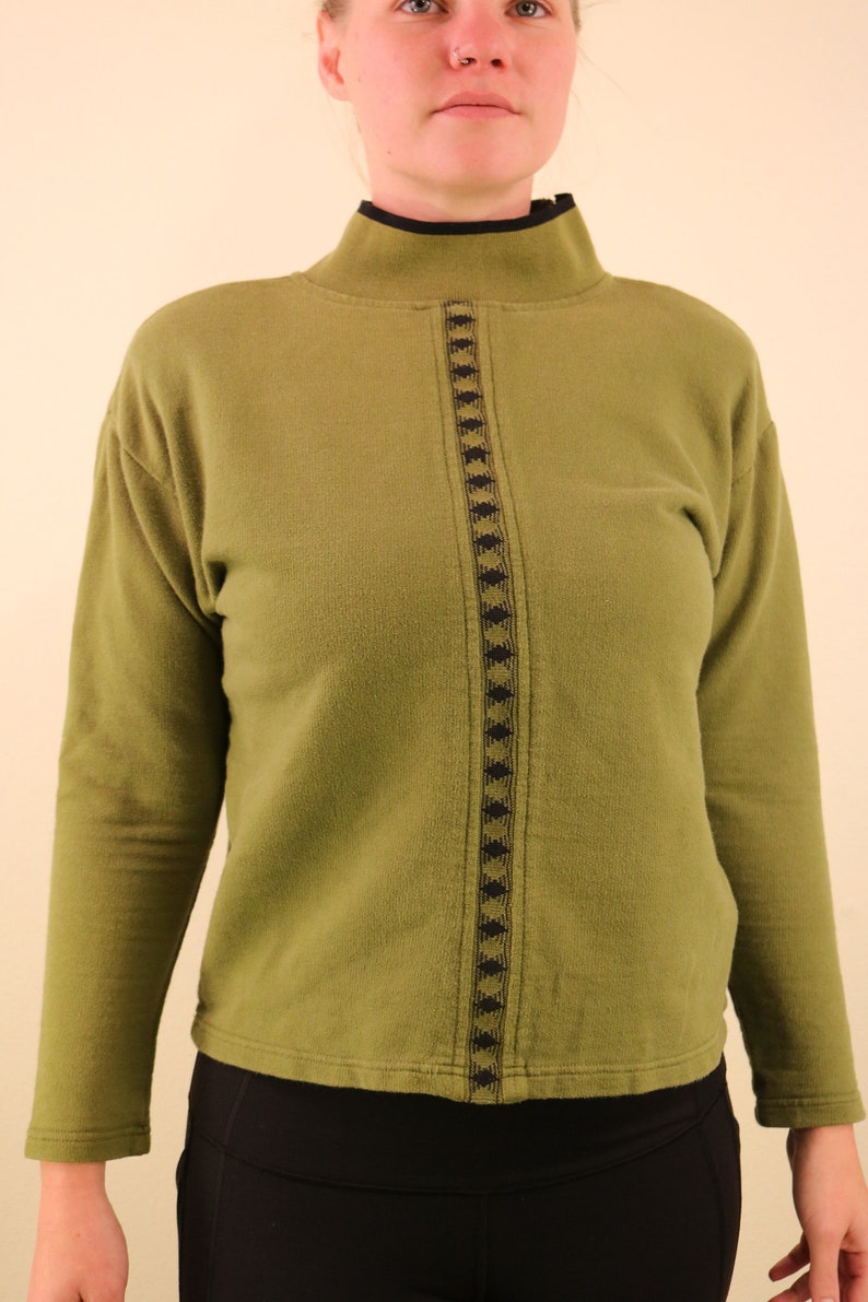 May include: A green mock neck sweater with a black and green geometric pattern down the front.
