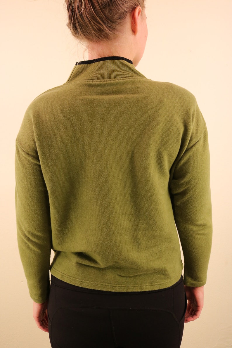 May include: A long-sleeved, olive green sweater with a mock neck and a zipper. The sweater is made of a soft, comfortable fabric.