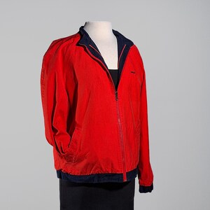 May include: A red zip-up jacket with a navy blue collar and trim. The jacket has a small logo on the chest and two front pockets. The jacket is displayed on a mannequin. The jacket is a size medium.