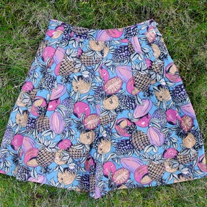 Op de afbeelding: Een blauwe short met een tropische fruitprint. De print bevat ananas, mango's en andere vruchten in tinten roze, geel en bruin.