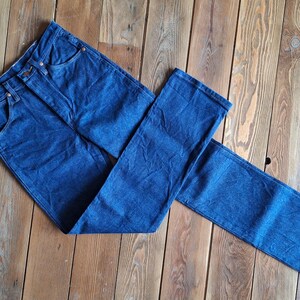 May include: A pair of dark blue denim jeans laid out on a wooden surface. The jeans are folded in half, with one leg on top of the other.