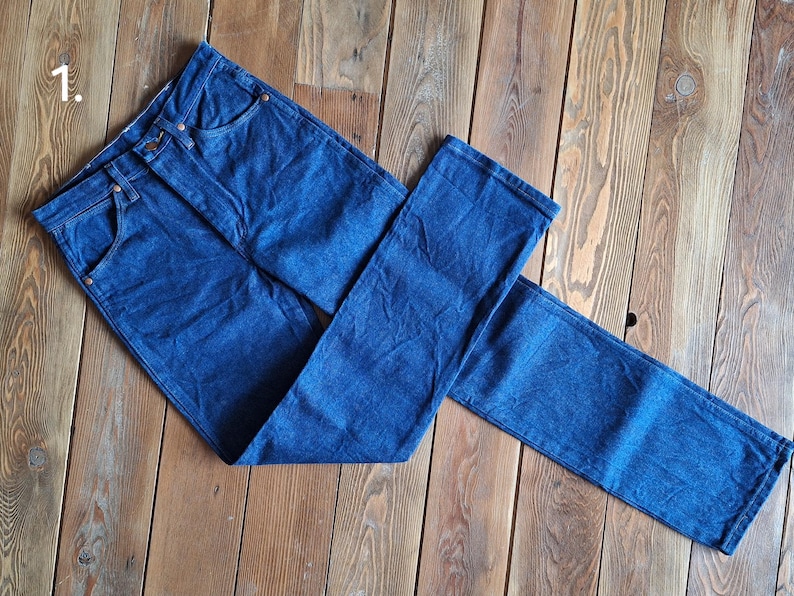 May include: A pair of dark blue denim jeans laid out on a wooden surface. The jeans are folded in half, with one leg on top of the other.