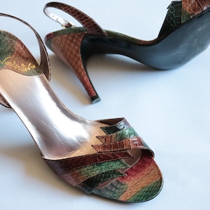 Puede incluir: Un par de sandalias de tacón de cuero marrón, verde y rojo con una correa de slingback. Las sandalias tienen un patrón de piel de serpiente y el nombre de la marca "Gloria Vanderbilt" está escrito en la plantilla.