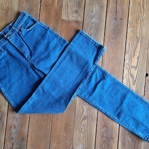 May include: A pair of blue denim jeans folded in half on a wooden surface. The jeans have a classic five-pocket style and a straight leg.