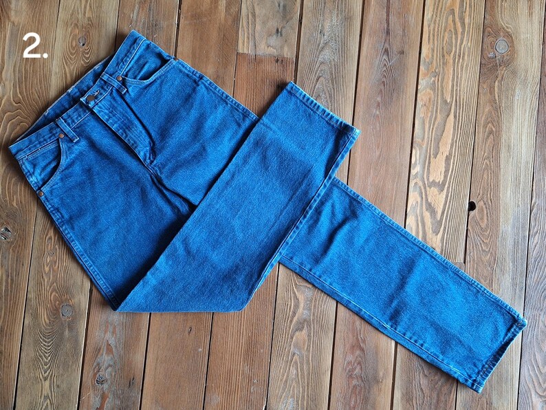 May include: A pair of blue denim jeans folded in half on a wooden surface. The jeans have a classic five-pocket style and a straight leg.