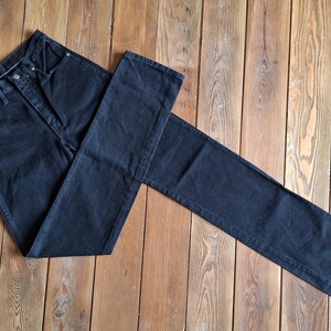 May include: A pair of dark blue denim jeans laid out on a wooden surface. The jeans are folded in half, with the front of the jeans facing up. The jeans have a classic five-pocket style.