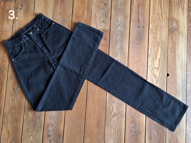 May include: A pair of dark blue denim jeans laid out on a wooden surface. The jeans are folded in half, with the front of the jeans facing up. The jeans have a classic five-pocket style.