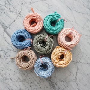 May include: Eight spools of cotton rope in various colors, including pink, blue, green, beige, and yellow. The spools are arranged in a circle on a white marble surface. The text "cotton + tree" is visible in the center of the image.