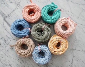 May include: Eight spools of cotton rope in various colors, including pink, blue, green, beige, and yellow. The spools are arranged in a circle on a white marble surface. The text "cotton + tree" is visible in the center of the image.
