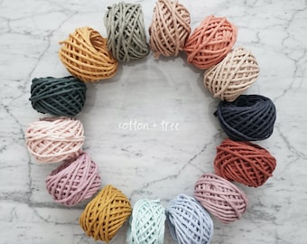 May include: A collection of 12 spools of cotton rope in various colors, including pink, blue, green, brown, and yellow. The spools are arranged in a circle on a white marble surface. The text "cotton + tree" is written in black on the surface.