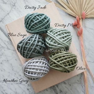 Op de afbeelding: Vijf bollen katoenen touw in verschillende tinten groen en grijs. De kleuren zijn gelabeld "Dusty Jade", "Dusty Mint", "Blue Sage", "Olive" en "Heather Grey".