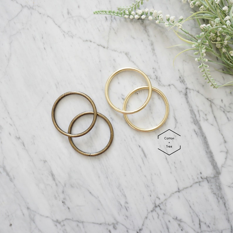 May include: Two sets of metal rings, one set is gold and the other is bronze. The rings are on a white marble surface.