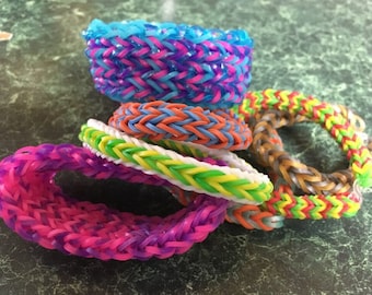 May include: A stack of colourful rubber band bracelets in various patterns, including pink, blue, green, yellow and orange.