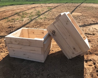 Peut inclure: Deux caisses en bois non finies, l'une ouverte et l'autre fermée, posées sur une surface sablonneuse. Les caisses sont en bois naturel de couleur brun clair.
