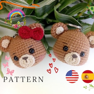 Puede incluir: Dos llaveros de osito de peluche de crochet marrón con ojos negros y un lazo rojo en uno. Los llaveros están sobre un fondo blanco con hojas verdes y corazones. El texto "PATTERN" está debajo de los osos. Las banderas de Estados Unidos y España están debajo del texto.