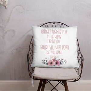 May include: White throw pillow with a floral design and the text "BEFORE I FORMED YOU IN THE WOMB I KNEW YOU. BEFORE YOU WERE BORN I SET YOU APART. JEREMIAH 1:5" in pink lettering.