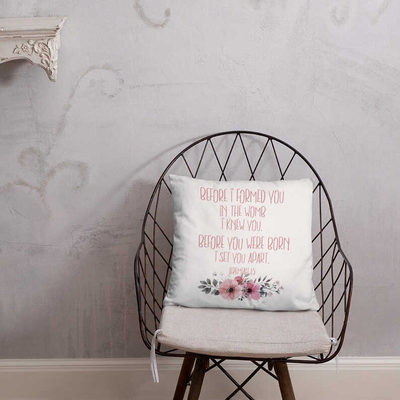 May include: White throw pillow with a floral design and pink text that reads "BEFORE I FORMED YOU IN THE WOMB I KNEW YOU. BEFORE YOU WERE BORN I SET YOU APART. JEREMIAH 1:5"