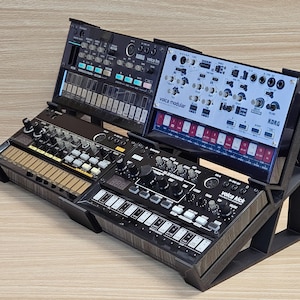 May include: A black synthesizer stand holding three Korg Volca synthesizers. The stand is angled, with the synthesizers at different heights. The synthesizers have various buttons, knobs, and keys. The text "Korg" and "Volca" are visible on the synthesizers.