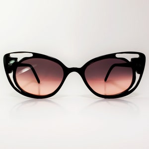 Puede incluir: Gafas de sol negras de ojo de gato con un diseño único de corte en el marco. Las lentes son de color degradado, pasando de oscuro a claro.
