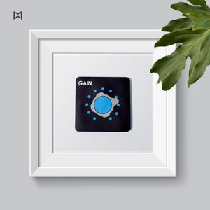 May include: A white framed picture with a black square sticker that says "GAIN" in white text. The sticker has a blue circle with a white outline in the centre and a ring of small blue dots around it.