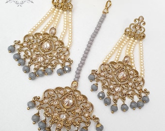 May include: A set of gold-tone earrings and a maang tikka with grey and white beads. The earrings feature a floral design and are accented with clear stones. The maang tikka is a long, beaded chain with a floral design at the top.