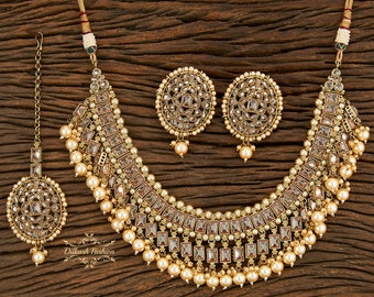 May include: A gold-tone necklace set with a layered design featuring clear stones and pearl accents. The set includes a matching pair of earrings.