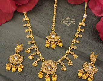 May include: A gold-tone necklace set with a square pendant, matching earrings, and a tikka. The jewelry is adorned with clear stones and has a traditional Indian design.