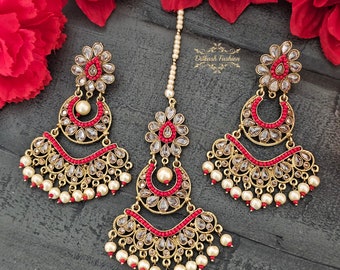 May include: A gold-tone Indian bridal jewelry set with red and white accents. The set includes a maang tikka, earrings, and a necklace.
