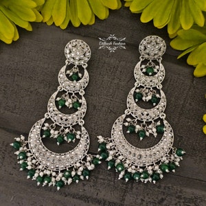 May include: Silver earrings with three crescent moon shapes, each decorated with small white stones. The earrings are accented with green beads and white pearls.