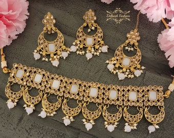 May include: A gold-tone necklace with white stones and a matching pair of earrings. The necklace has a choker style with a row of square stones and a row of crescent moons. The earrings are also crescent moon shaped with white stones.