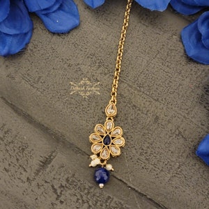 May include: Gold chain with a blue and white flower pendant and white pearl accents. The pendant has a blue gemstone in the center.