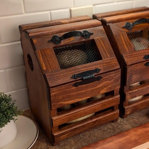 May include: Two wooden storage bins with a dark stain. Each bin has a slatted front and a mesh-covered window. Black metal handles and hinges add detail. The bins are designed for kitchen storage.