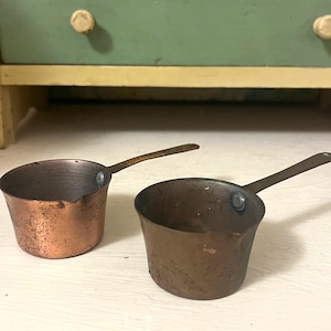 May include: Two small copper pots with handles. The pots have a rustic, aged look.