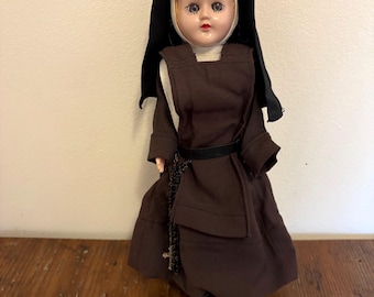 Muñeca religiosa católica de los años 50 con rostro de plástico, vestida con hábito marrón y negro, rosario, cruz y crucifijo.