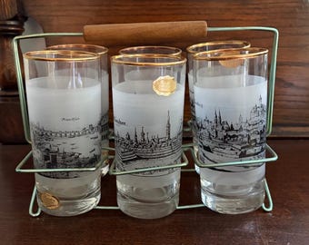 Juego vintage de los años 50 de 6 vasos altos de cristal esmerilado con paisajes urbanos alemanes y bordes chapados en oro, en su soporte de alambre original. Recuerdo de bar de mediados de siglo.