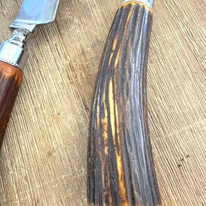 Puede incluir: Primer plano de un cuchillo para trinchar y un utensilio para servir. Las hojas son plateadas y los mangos son marrones y amarillos con un dise&ntilde;o texturizado y acanalado. Las hojas reflejan la luz. Utensilios para trinchar y servir.