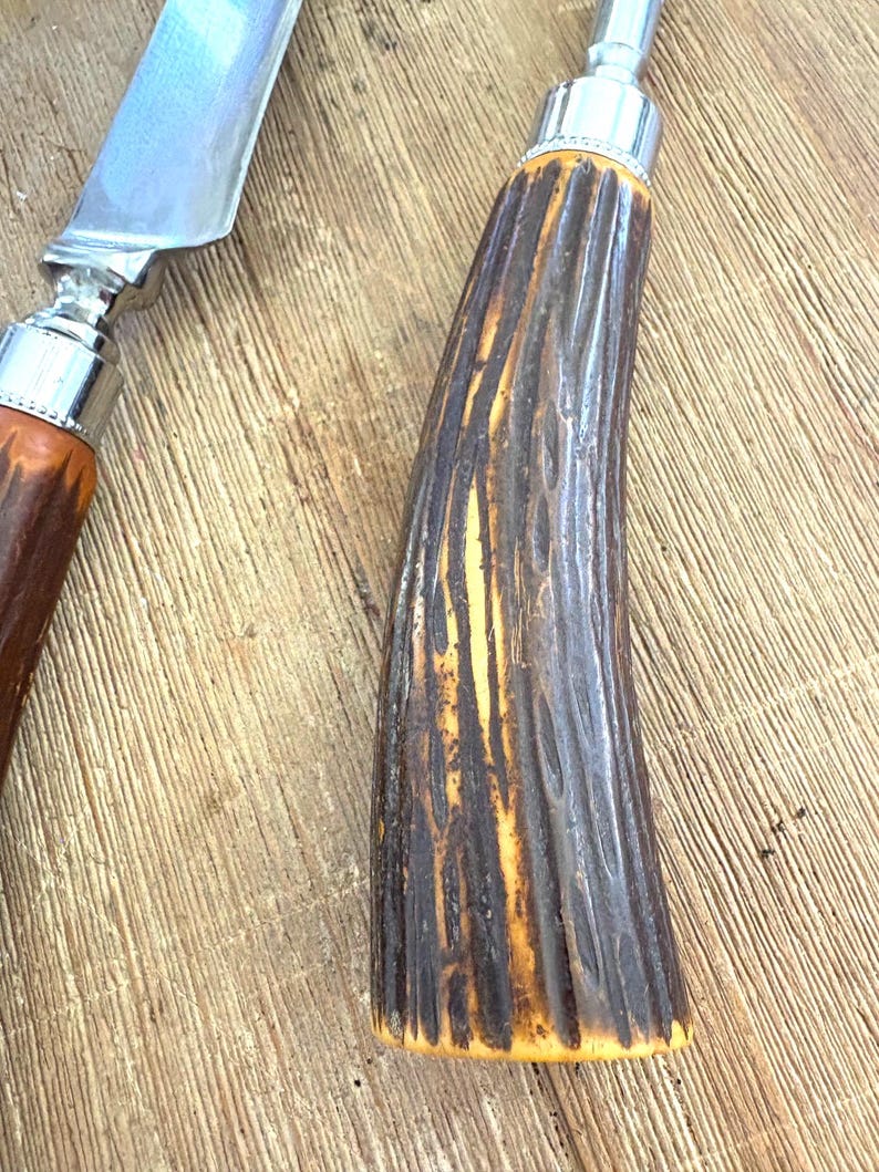Puede incluir: Primer plano de un cuchillo para trinchar y un utensilio para servir. Las hojas son plateadas y los mangos son marrones y amarillos con un dise&ntilde;o texturizado y acanalado. Las hojas reflejan la luz. Utensilios para trinchar y servir.