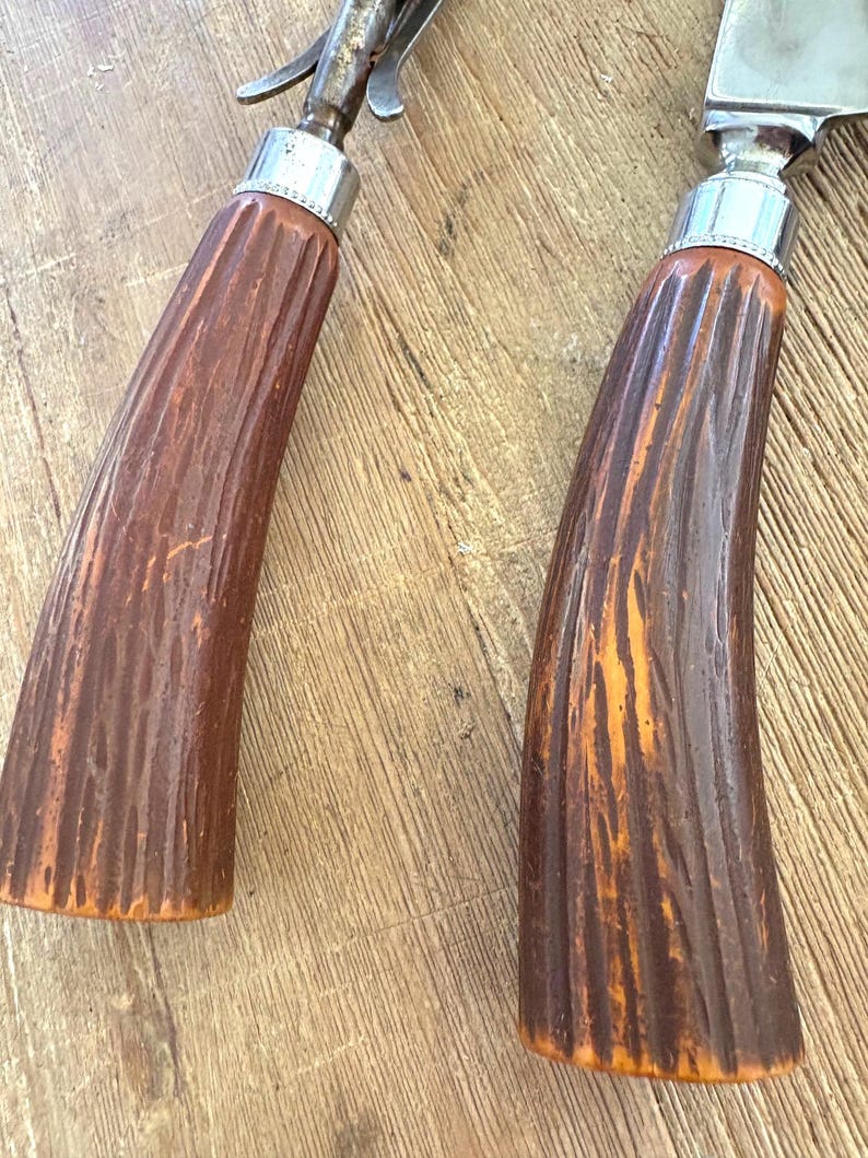 Puede incluir: Primer plano de dos cuchillos de trinchar antiguos. Los mangos son de color marr&oacute;n oscuro con un dise&ntilde;o texturizado y acanalado. Las virolas met&aacute;licas son plateadas y las hojas son visibles. Los cuchillos est&aacute;n sobre una superficie de madera.