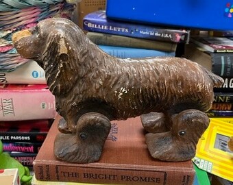May include: A brown, wooden toy dog with wheels. The dog has a long snout and floppy ears. The wheels are black and have a rubber tire.