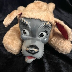 May include: A plush toy dog with a gray face and brown fur. The dog has large, black eyes and a pink tongue sticking out.