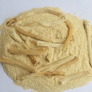 May include: A pile of light brown powder with several long, thin, light brown sticks on top. The powder and sticks are likely a type of herbal supplement.