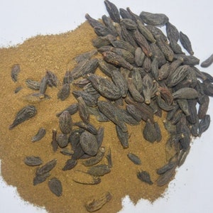 May include: A pile of brown powder with dark brown seeds scattered on top. The powder is likely a spice or herb.