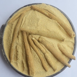 May include: A close-up of a black bowl filled with light brown powder and several long, thin, light brown sticks. The sticks are arranged in a radial pattern, with the tips pointing towards the center of the bowl.