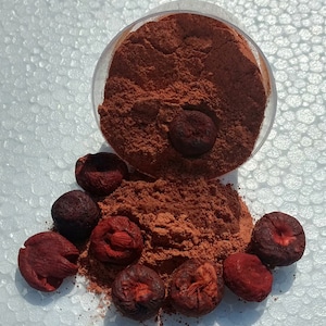 May include: A bowl of red powder with a pile of dried red berries scattered around it.