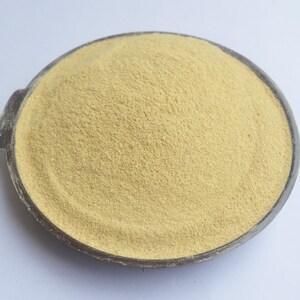 May include: A close-up of a light yellow powder in a black bowl. The powder is finely ground and has a smooth texture.